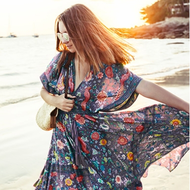 Woman in floral dress walking on the beach at sunset, promoting affordable fashion.